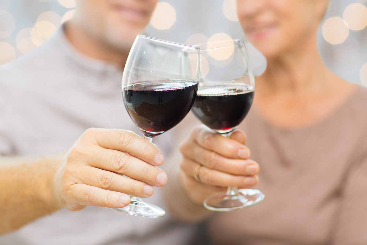 Close up of happy senior couple clinking glasses with red wine over lights background-Wellington Senior Living