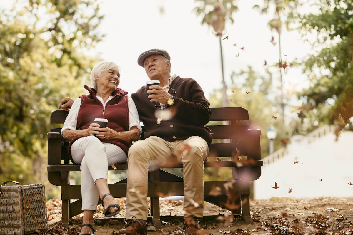 Relaxed senior couple on picnic sitting on park bench talking and having coffee