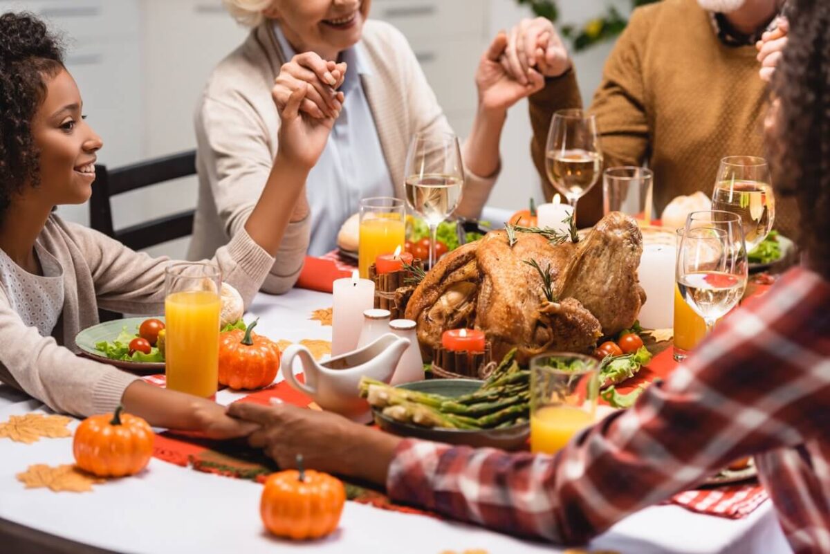 multigenerational family holding hands at table healthy food alternatives for thanksgiving dinner